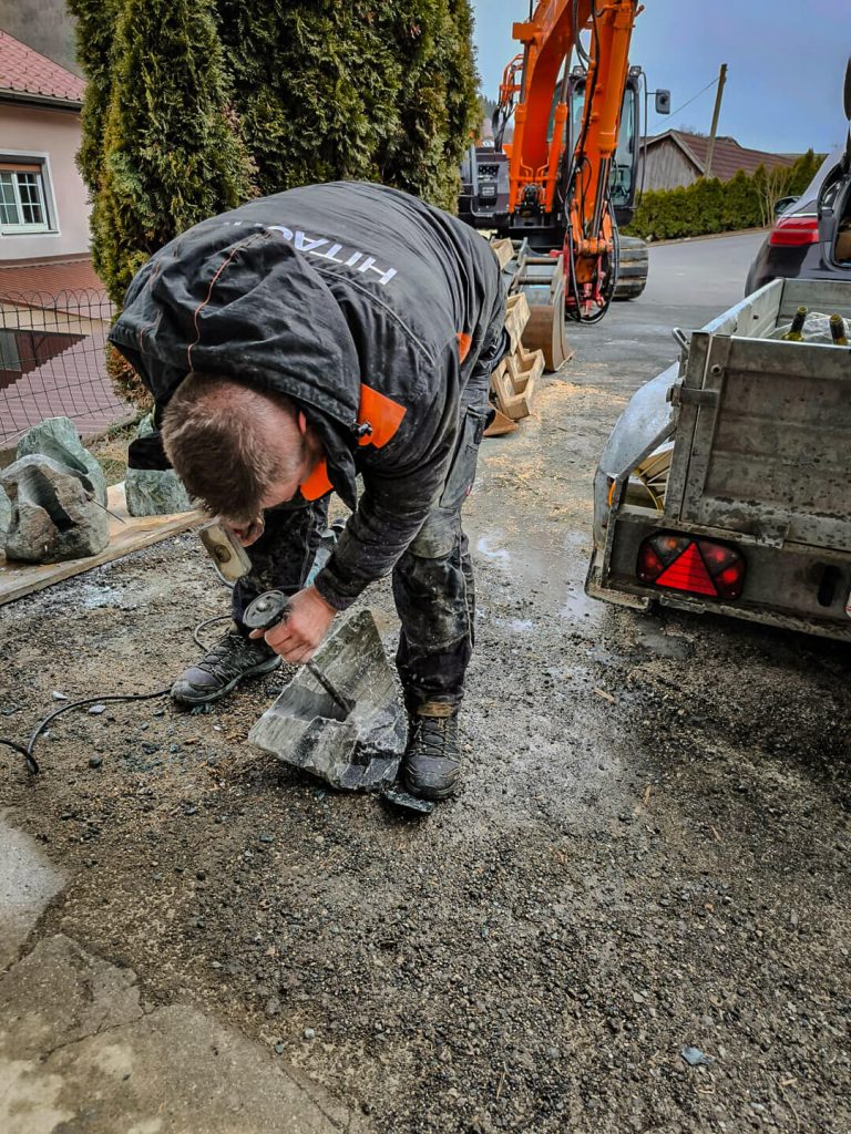 Handwerker bearbeitet Naturstein mit Winkelschleifer zur Herstellung eines Weinständers.