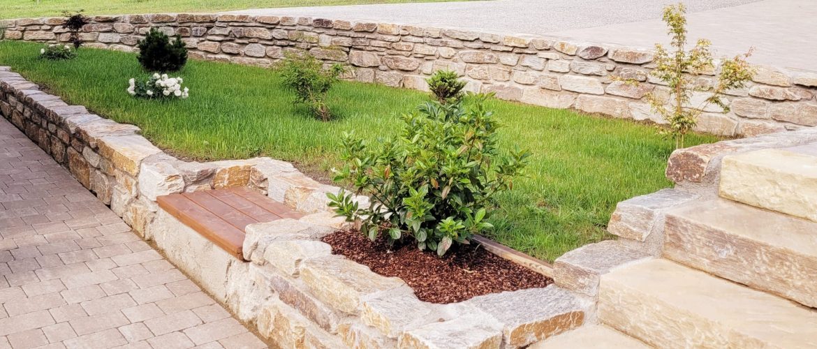 Garten mit Steinmauern, grünem Rasen, kleinen Sträuchern und Steinstufen.