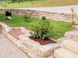 Garten mit Steinmauern, grünem Rasen, kleinen Sträuchern und Steinstufen.