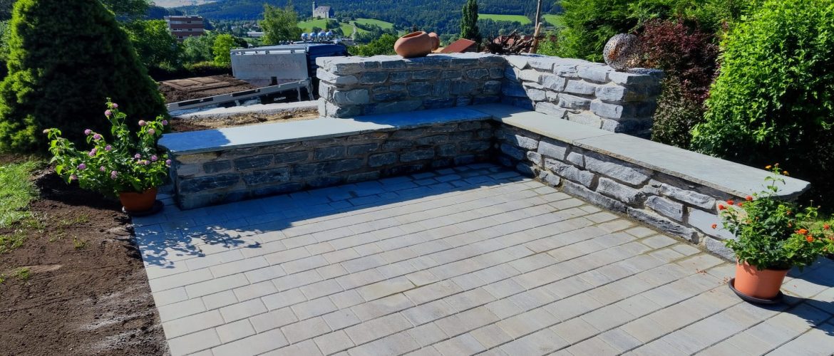 Terrasse mit Schieferstein-Sitzbank, Pflasterboden und Blumenkübeln.