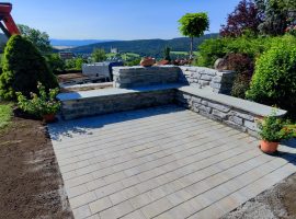 Terrasse mit Schieferstein-Sitzbank, Pflasterboden und Blumenkübeln.