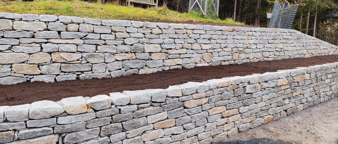 Lange Natursteinmauer mit Hofer-Stein und vorbereiteten Pflanzflächen.