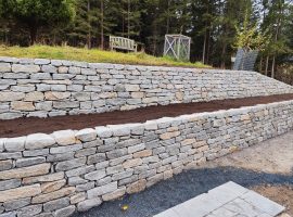 Lange Natursteinmauer mit Hofer-Stein und vorbereiteten Pflanzflächen.