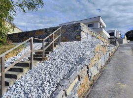 Stützmauer aus blauem Schiefer mit Treppe und Holzgeländer.