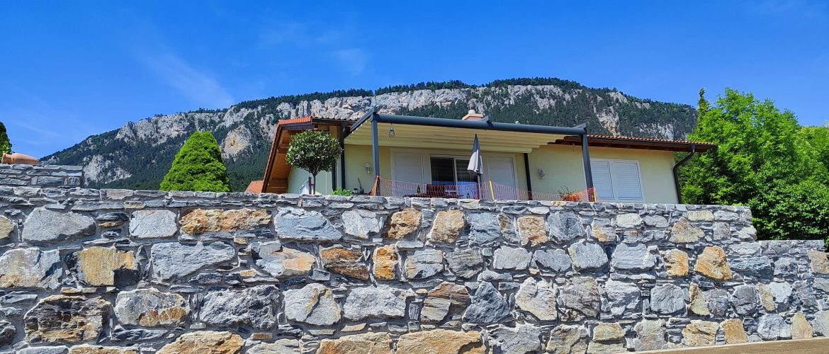 Blaue Schiefermauer in Beton vor Haus mit Blick auf Bergkulisse.