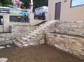 Gartengestaltung mit Natursteinmauer aus Gneis und Blockstufen in einem strukturierten Außenbereich