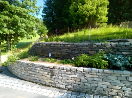 Abgestufte Natursteinmauer aus Gneis in einem gepflegten Garten mit Hanglage